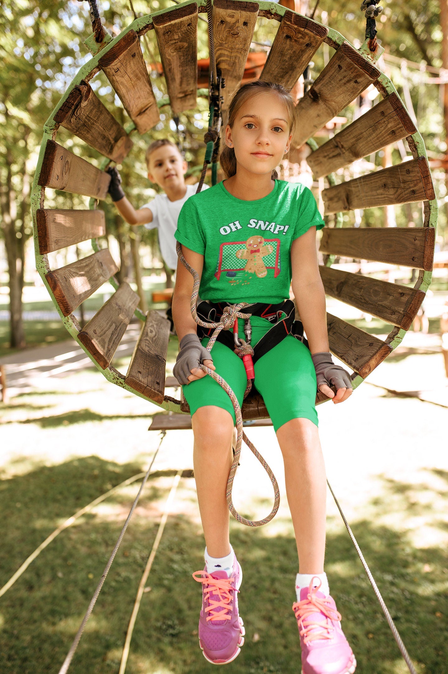 Girl wearing a heather kelly t-shirt. It says oh snap with the graphic of a gingerbread man with a broken leg in front of a hockey net. There is a puck in front.