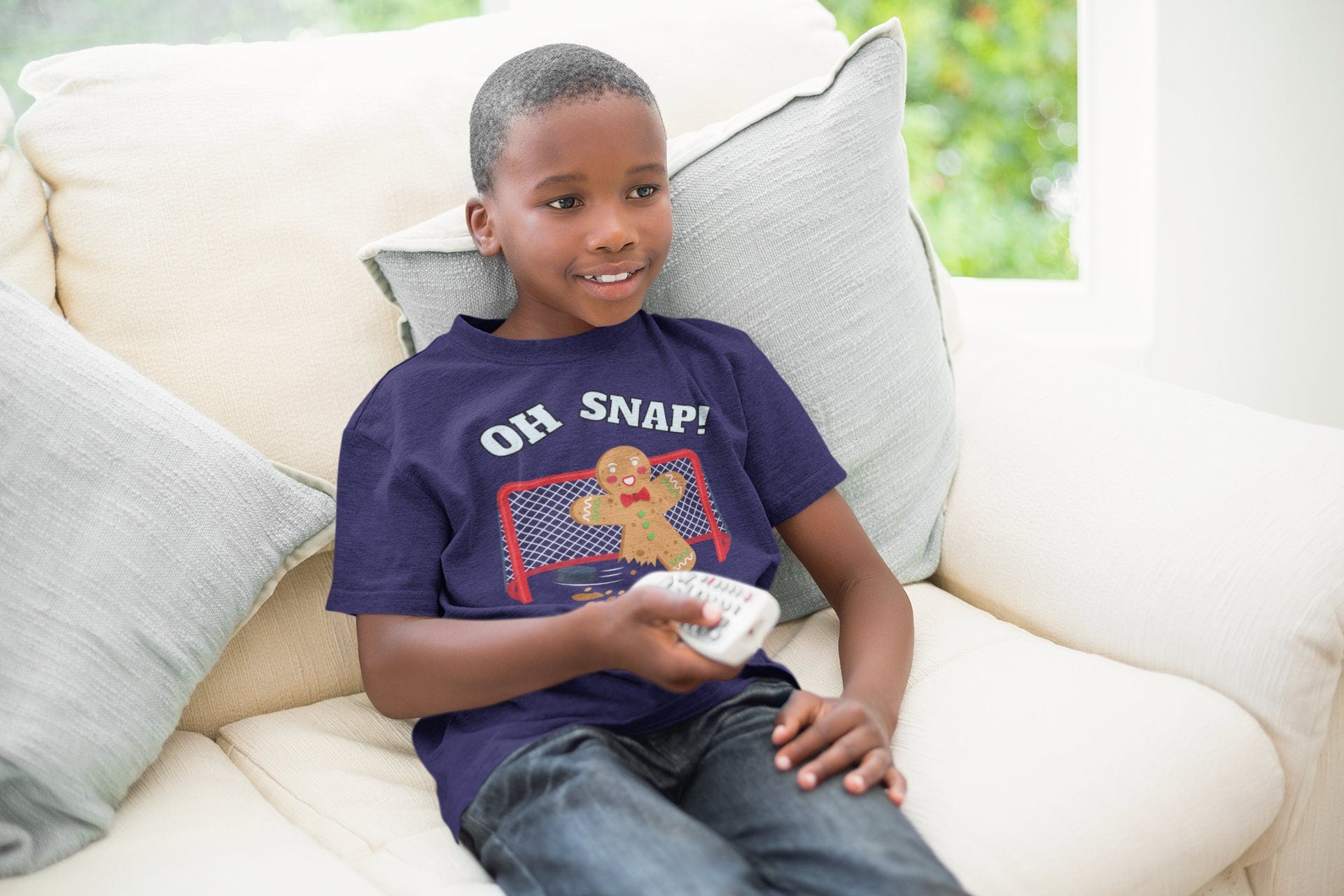 Boy wearing a heather navy t-shirt. It says oh snap with the graphic of a gingerbread man with a broken leg in front of a hockey net. There is a puck in front.