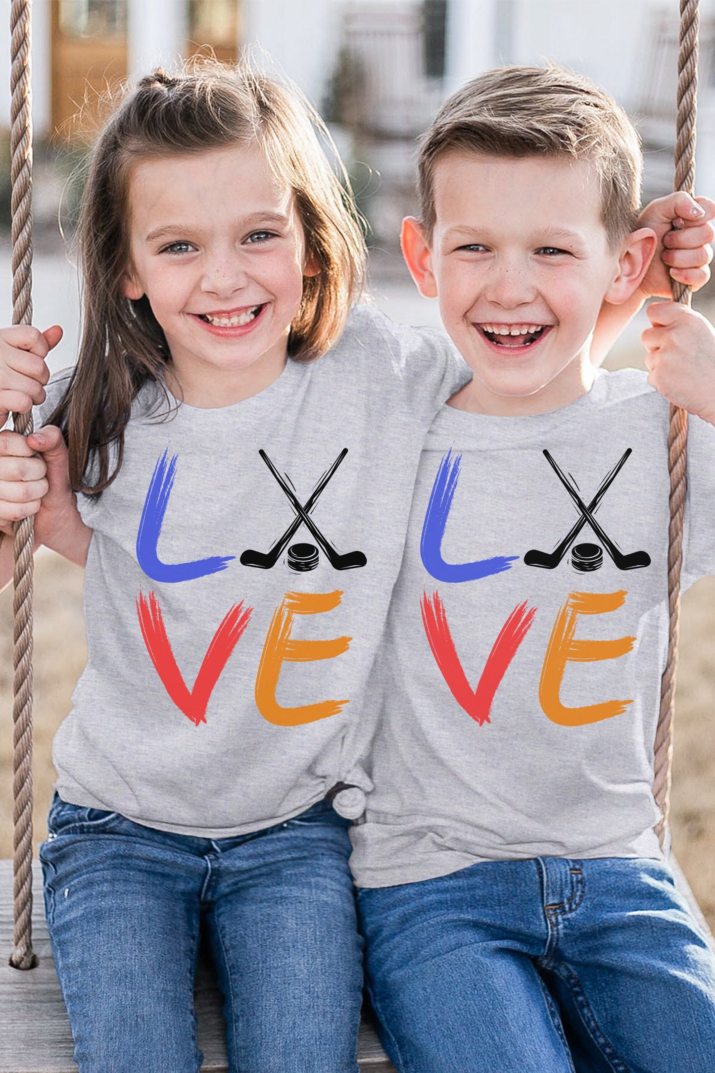 Girl and boy wearing an athletic heather Bella and Canvas 3001Y crewneck youth t-shirt. It says love in a brushed paint font. The o is replaced with two crossed hockey sticks and a hockey puck.