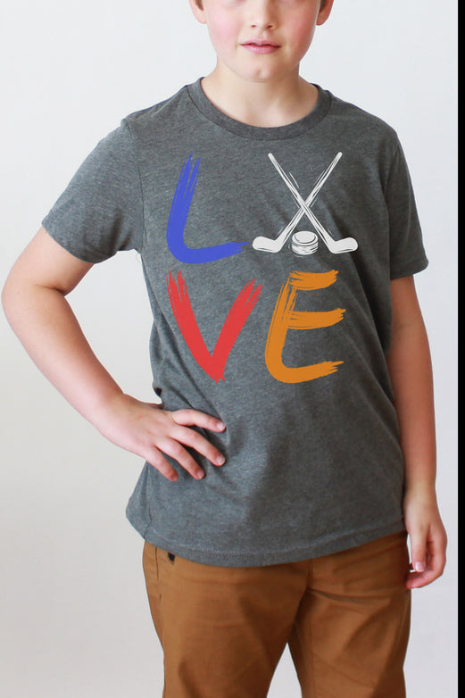 Girl wearing a deep heather Bella and Canvas 3001Y crewneck youth t-shirt. It says love in a brushed paint font. The o is replaced with two crossed hockey sticks and a hockey puck.