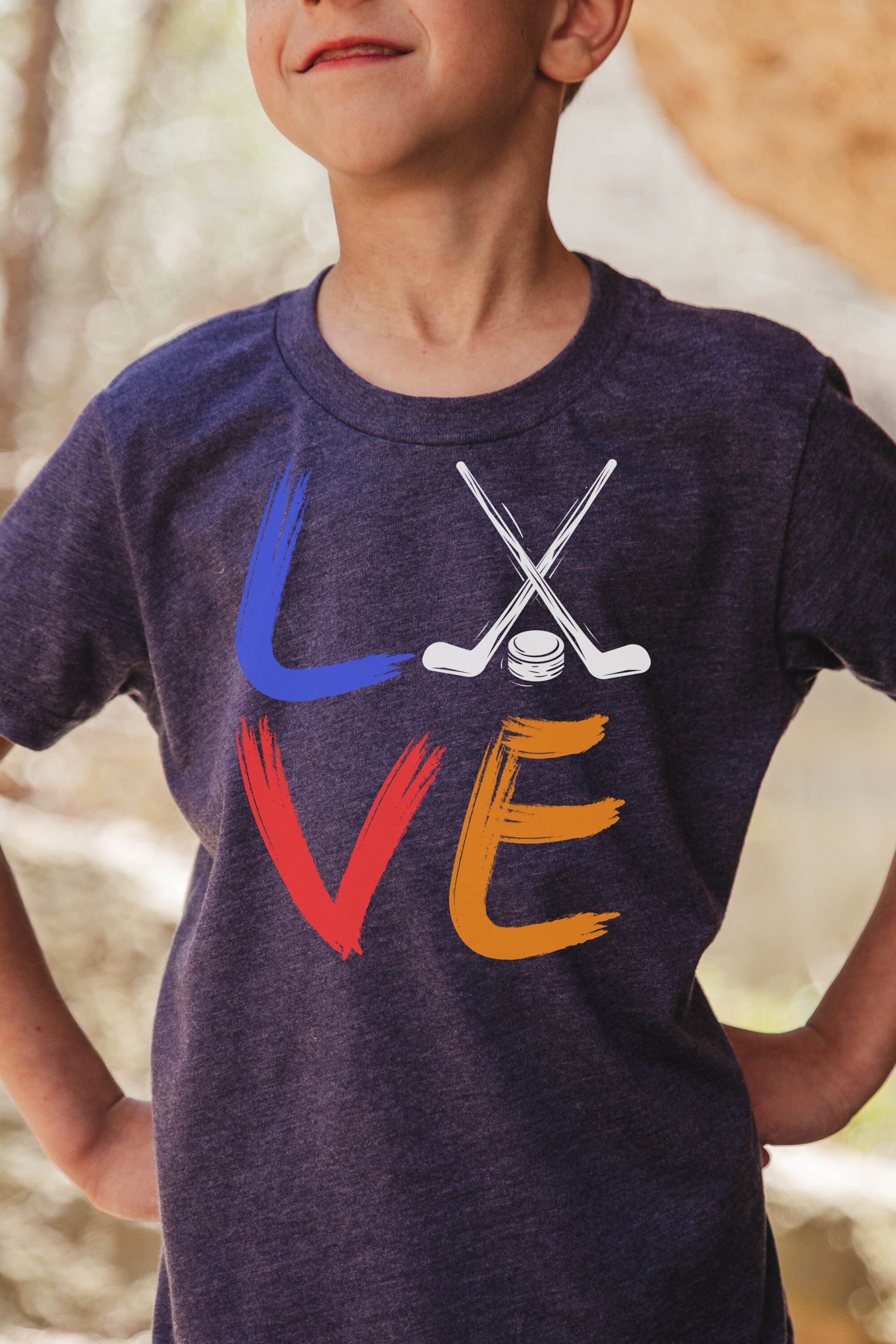 Girl wearing a heather navy Bella and Canvas 3001Y crewneck youth t-shirt. It says love in a brushed paint font. The o is replaced with two crossed hockey sticks and a hockey puck.