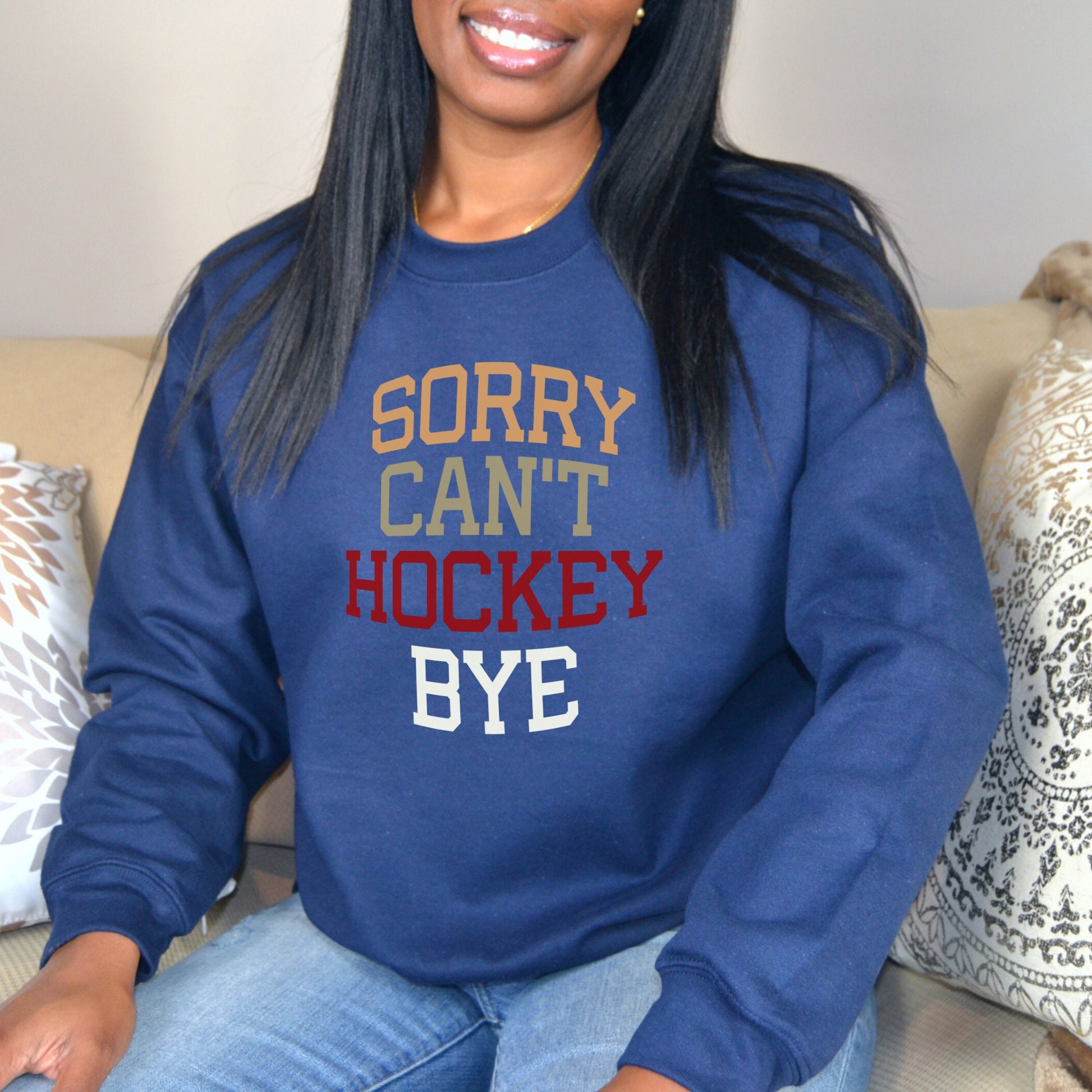 Smiling woman wearing a navy Gildan 18000 unisex crewneck sweatshirt. It says sorry cant hockey bye in different colored font. The words are bold and lined up vertically.