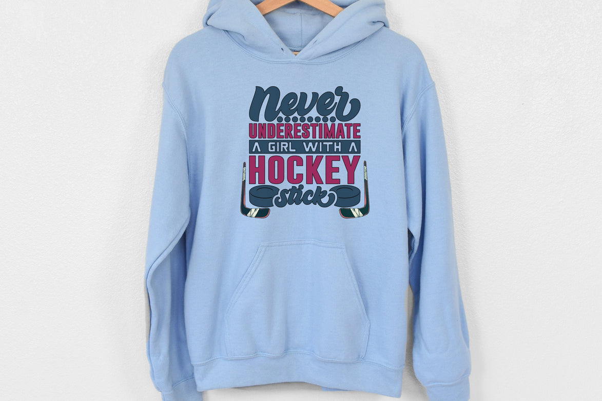 Light blue Gildan 18500 unisex crewneck sweatshirt. It says never underestimate a girl with a hockey stick in dark blue and hot pink. There are two pucks beside the word stick. There are hockey sticks on either side of the text.