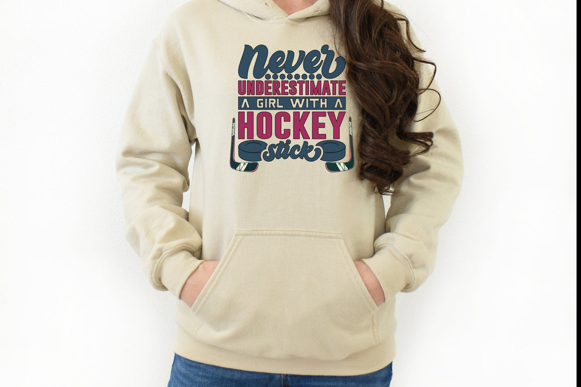 Sand Gildan 18500 unisex crewneck sweatshirt. It says never underestimate a girl with a hockey stick in dark blue and hot pink. There are two pucks beside the word stick. There are hockey sticks on either side of the text.