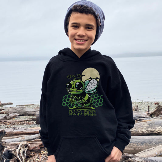 Boy wearing a Gildan 18500B youth hoodie. It has a drawing of a green and black zombie bee in the middle with a moon with bats and green honeycomb behind it. It says zom-bee at the bottom in a green drippy font.