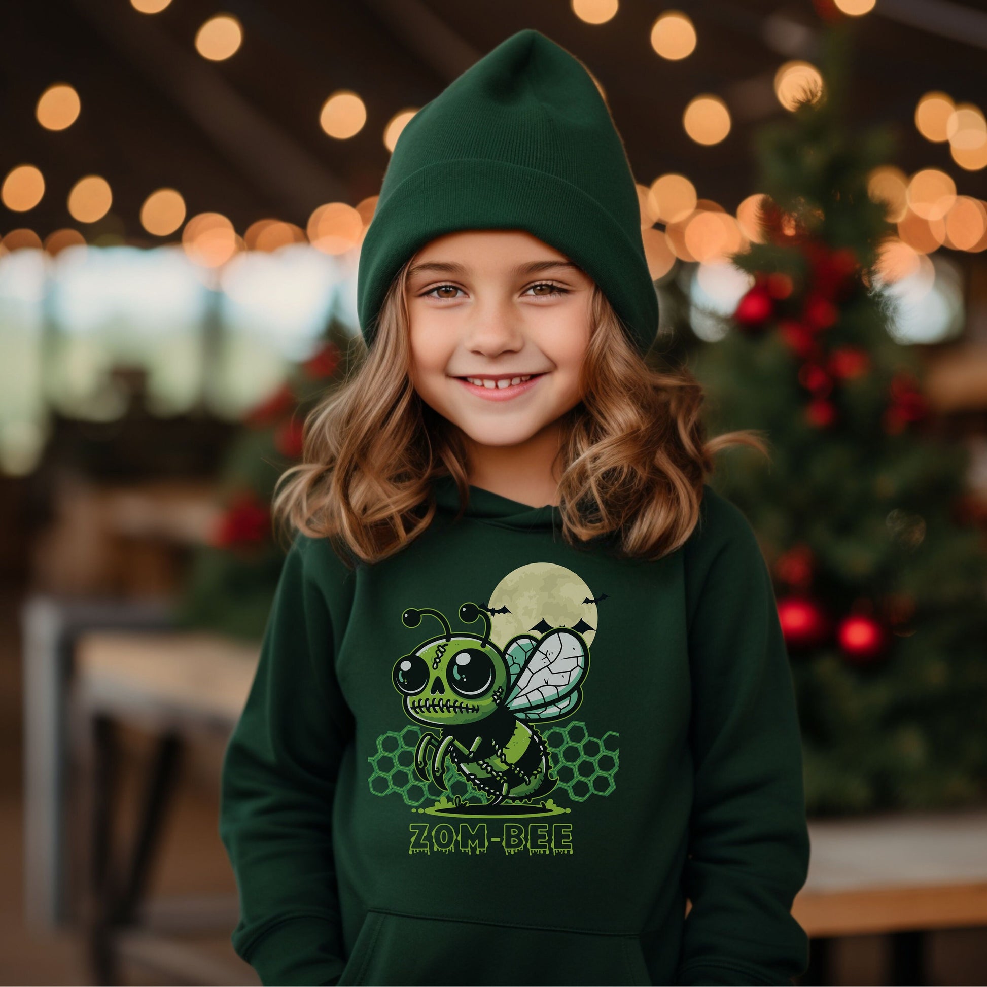 Girl wearing a forest Gildan 18500B youth hoodie. It has a drawing of a green and black zombie bee in the middle with a moon with bats and green honeycomb behind it. It says zom-bee at the bottom in a green drippy font.