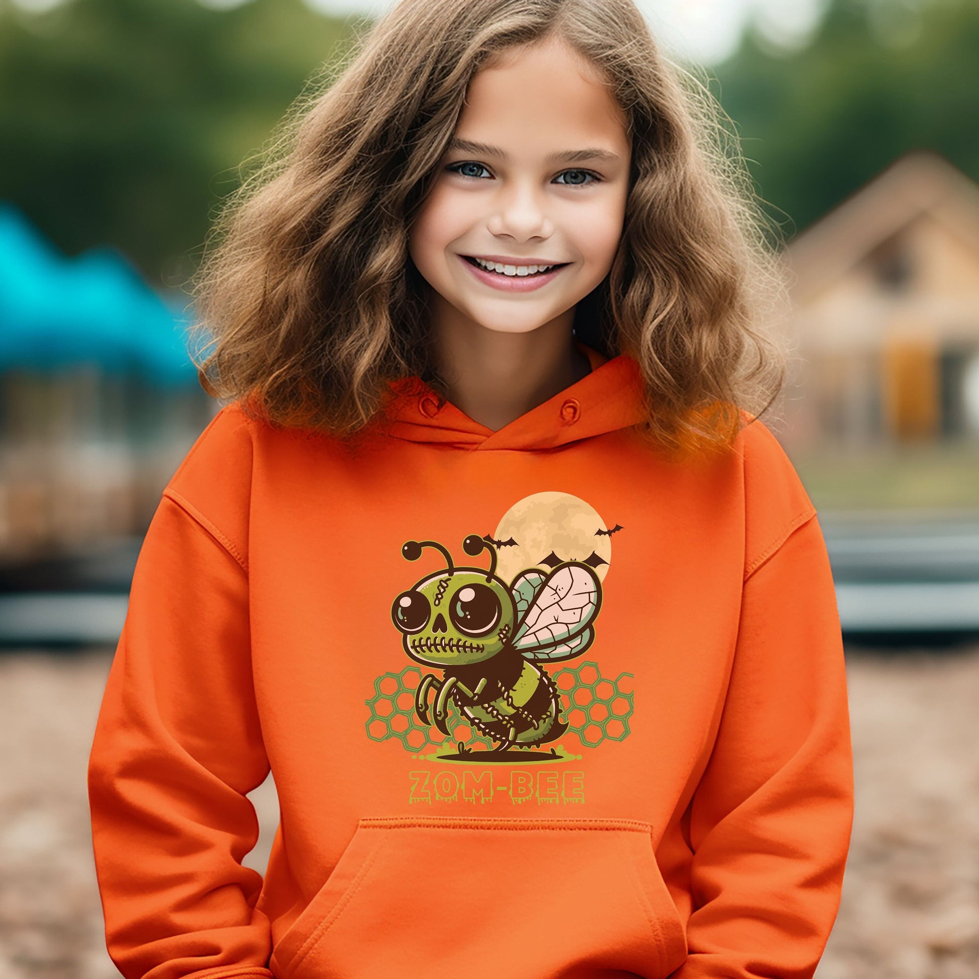 Girl wearing an orange Gildan 18500B youth hoodie. It has a drawing of a green and black zombie bee in the middle with a moon with bats and green honeycomb behind it. It says zom-bee at the bottom in a green drippy font.