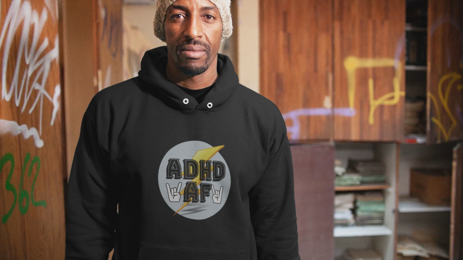 Video on a man in a premium unisex black hoodie that says adhd af in a room with graffitied walls